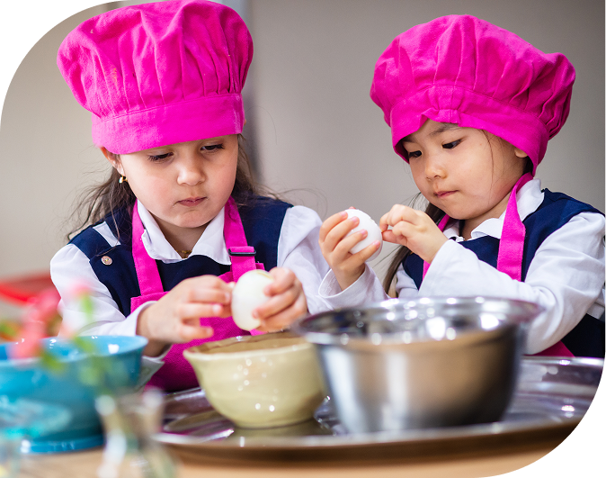 Two children cooking together wearing pink hats.